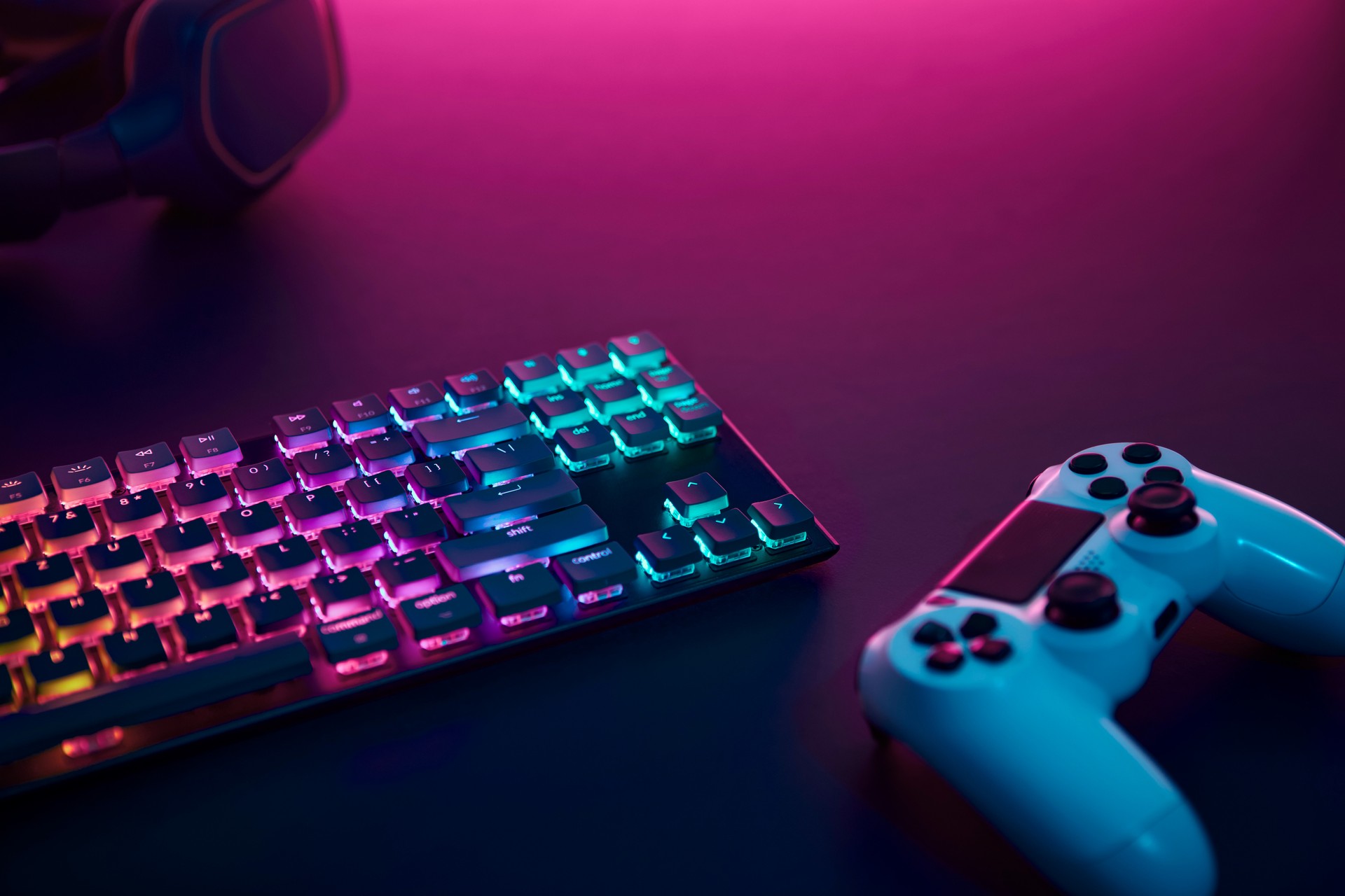 Rainbow color backlighted gaming keyboard, controller and stereo headphones. Purple light from top.